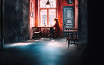 A person sits alone at a table by a sunlit window in a cozy, dimly lit café, working or reading, with empty chairs and tables around them and warm light casting long shadows on the floor.